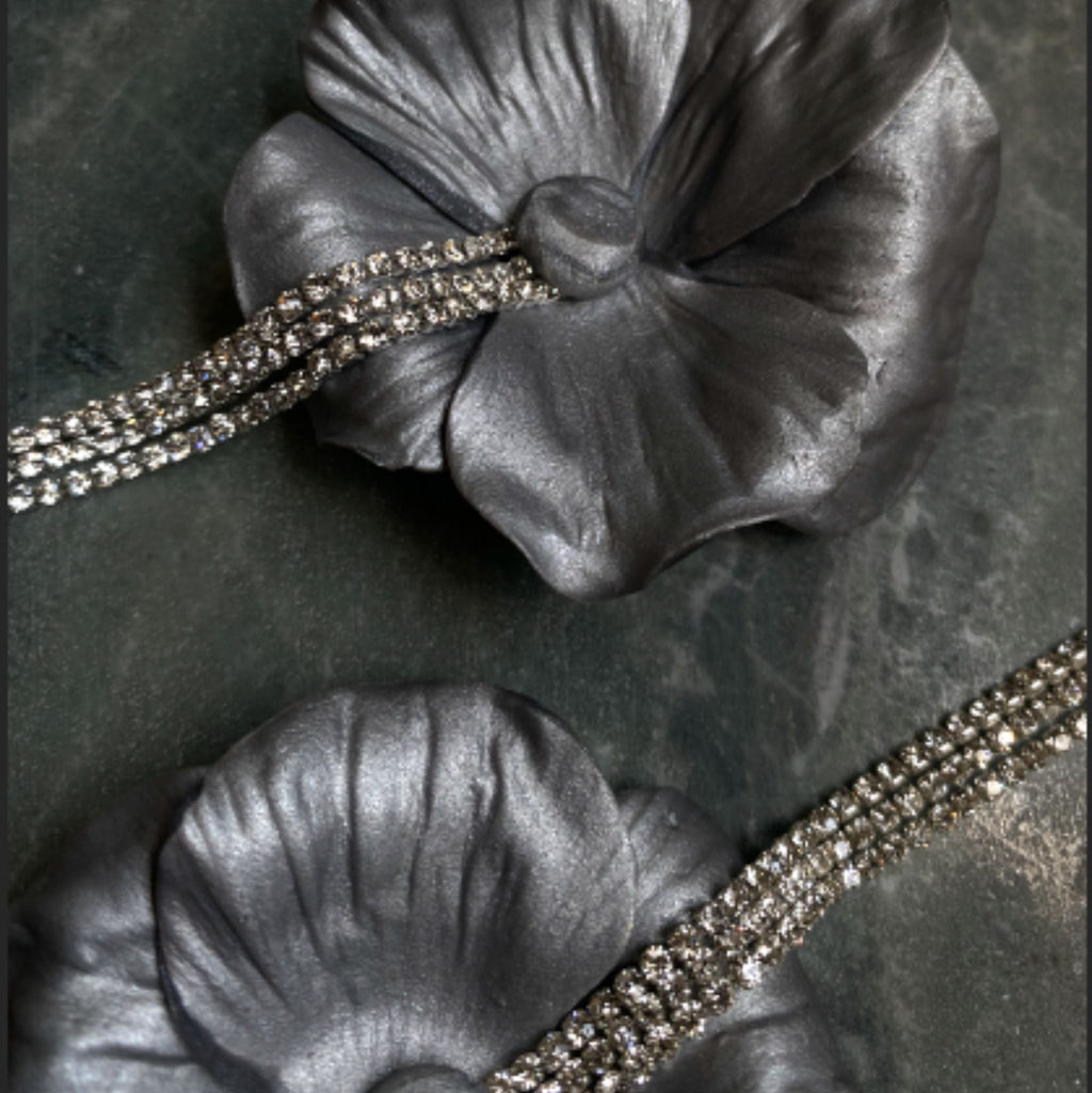 Gray floral brooch with rhinestone accents on a dark textured background