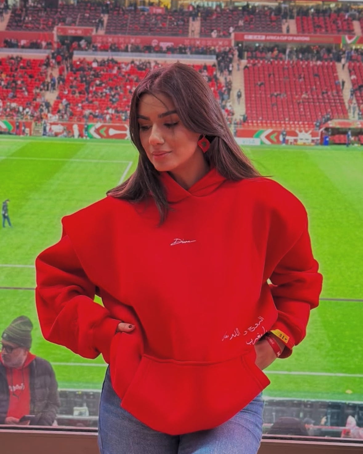 Person wearing a red hoodie with a logo in a stadium setting