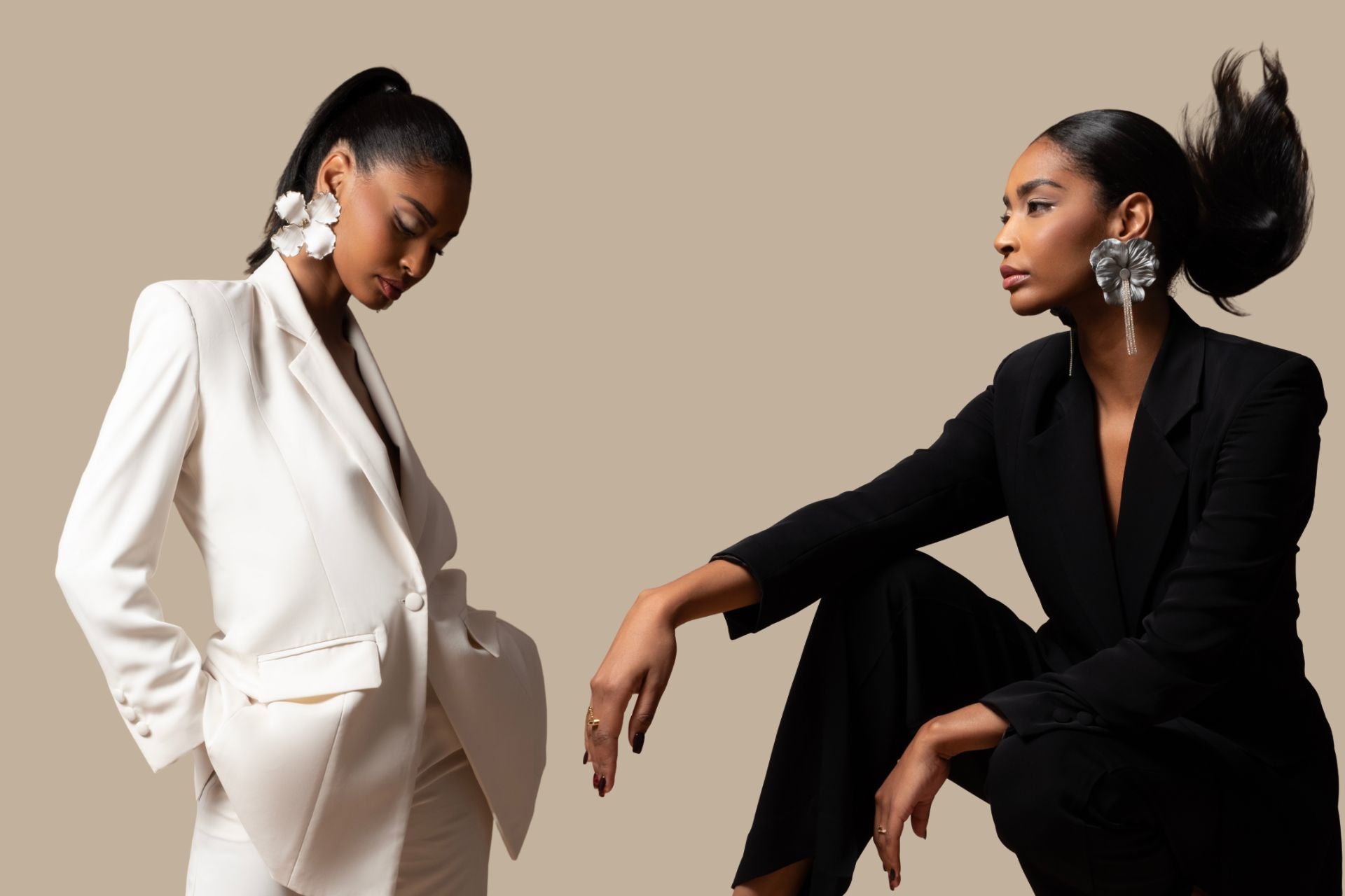 Two women in formal suits wearing statement earrings against a beige background